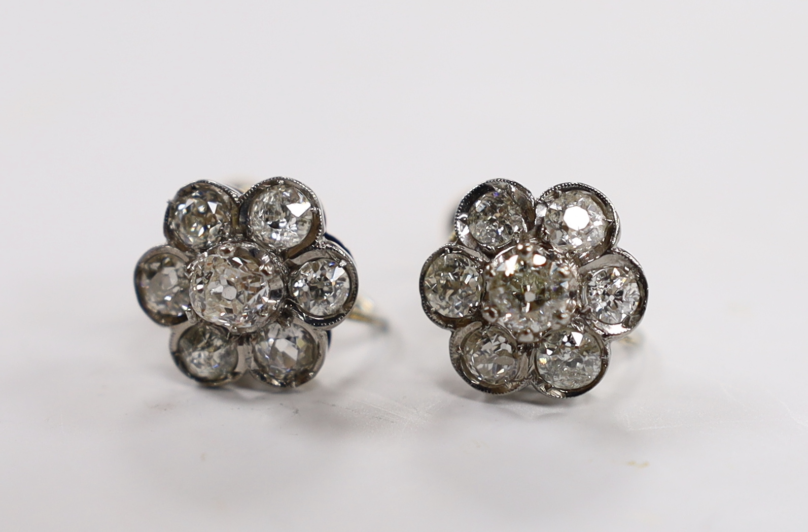 A pair of white metal and seven stone diamond set flower head cluster ear clips, 12mm, gross 4.9 grams.